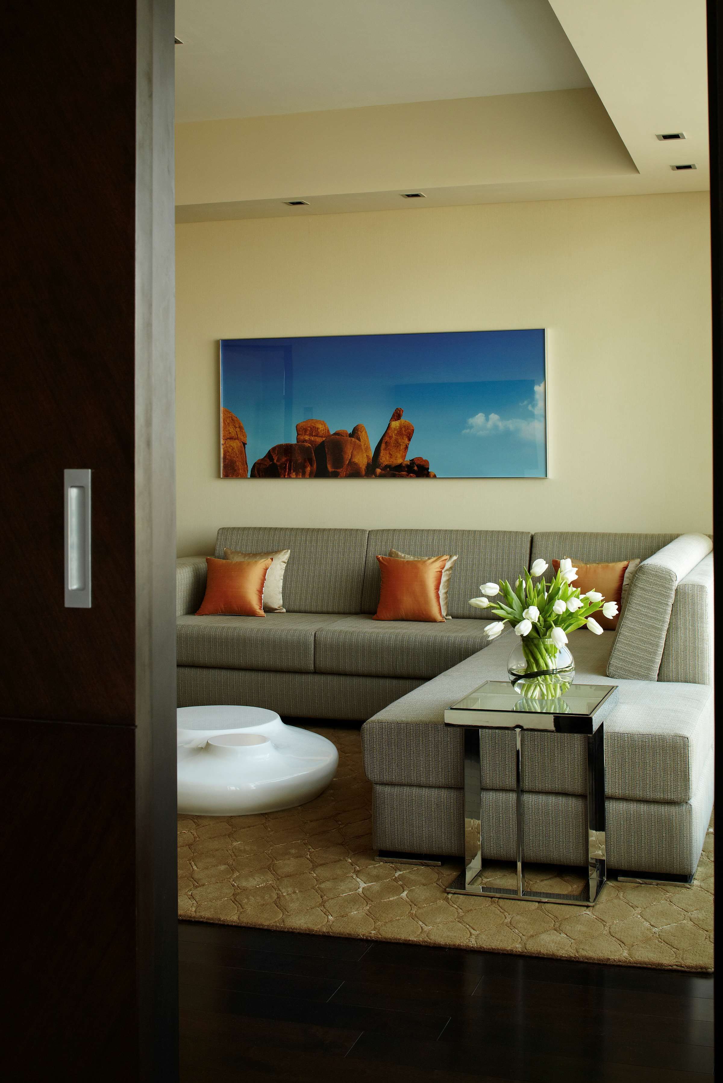 A modern living room with a grey sofa, a glass coffee table, and a painting of rock formations on the wall.