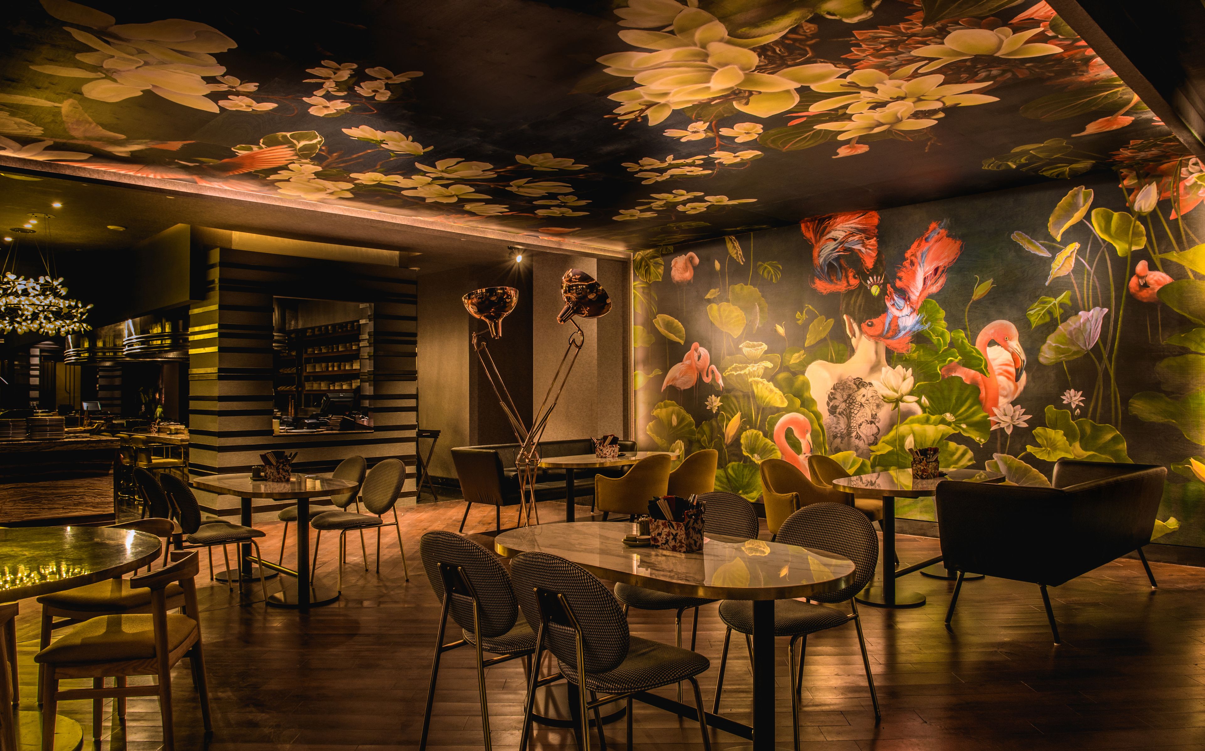 A restaurant with a mural of flowers and birds on the wall, wooden tables and chairs, and a bar area with shelves.