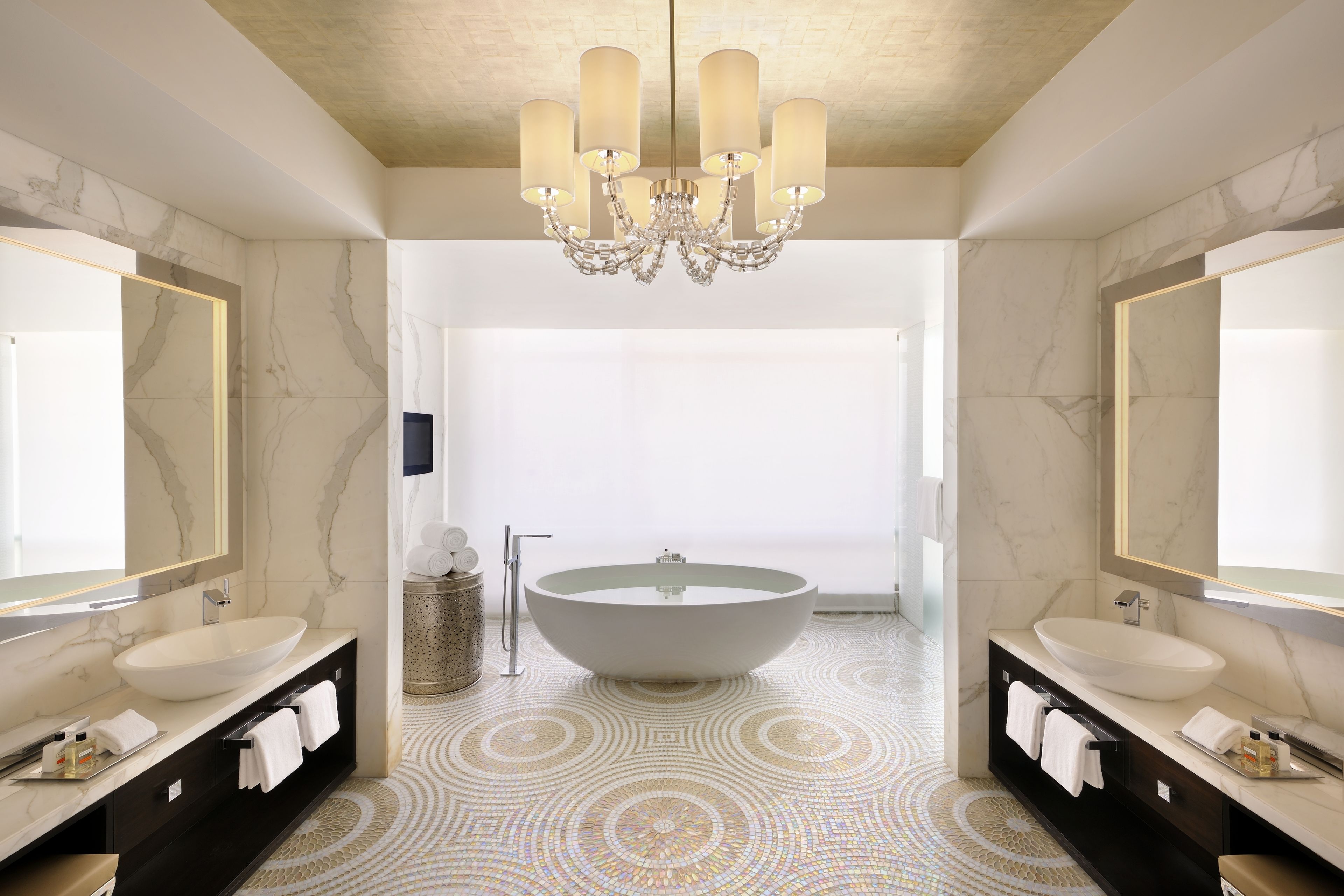 A modern bathroom with a large freestanding bathtub, two sinks, and a chandelier.