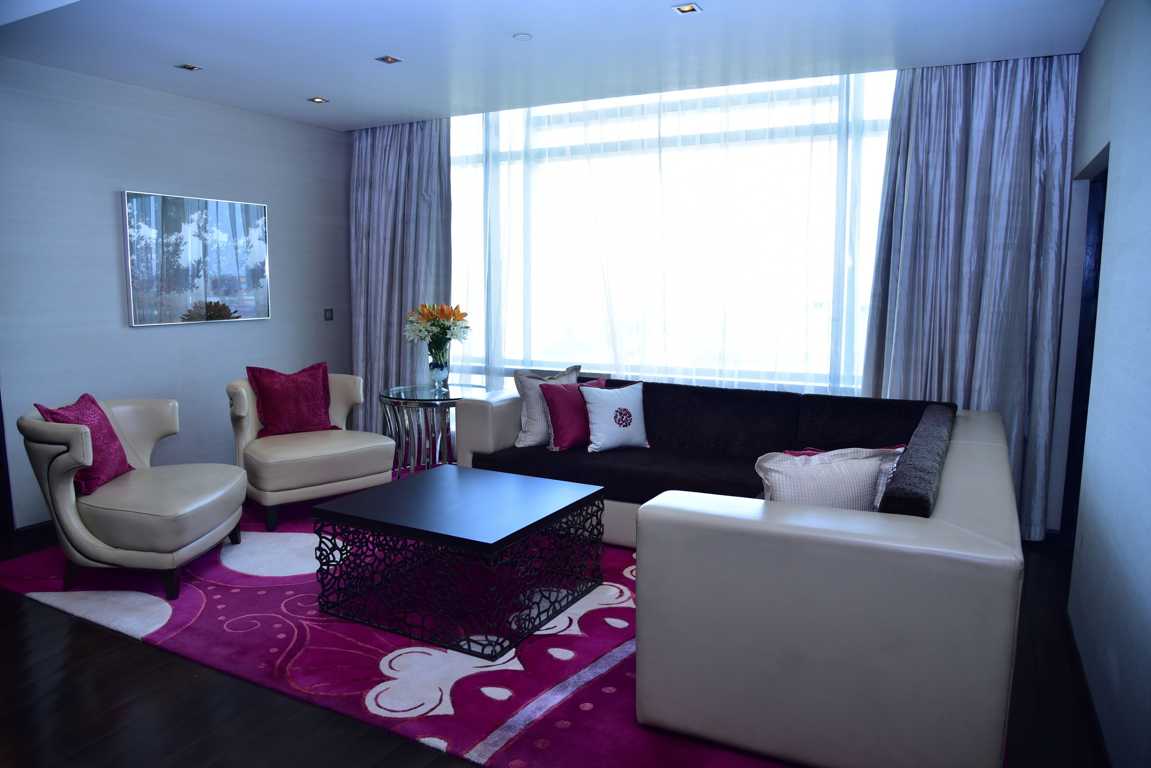 A modern living room with a sofa, two armchairs, a coffee table, and a painting on the wall.