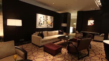 A modern hotel lobby with a sofa, ottoman, chairs, a coffee table, and artwork on the walls.
