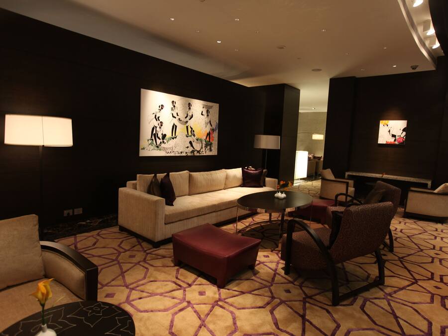 A modern hotel lobby with a sofa, ottoman, chairs, a coffee table, and artwork on the walls.