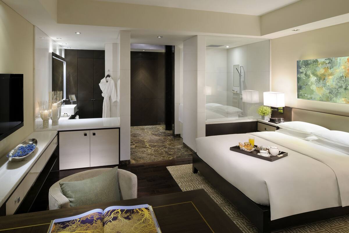 Une chambre d’hôtel moderne dotée d’un grand lit, d’un coin salon avec un fauteuil, d’un bureau avec un ordinateur, d’une salle de bain avec un miroir et d’un tableau accroché au mur.