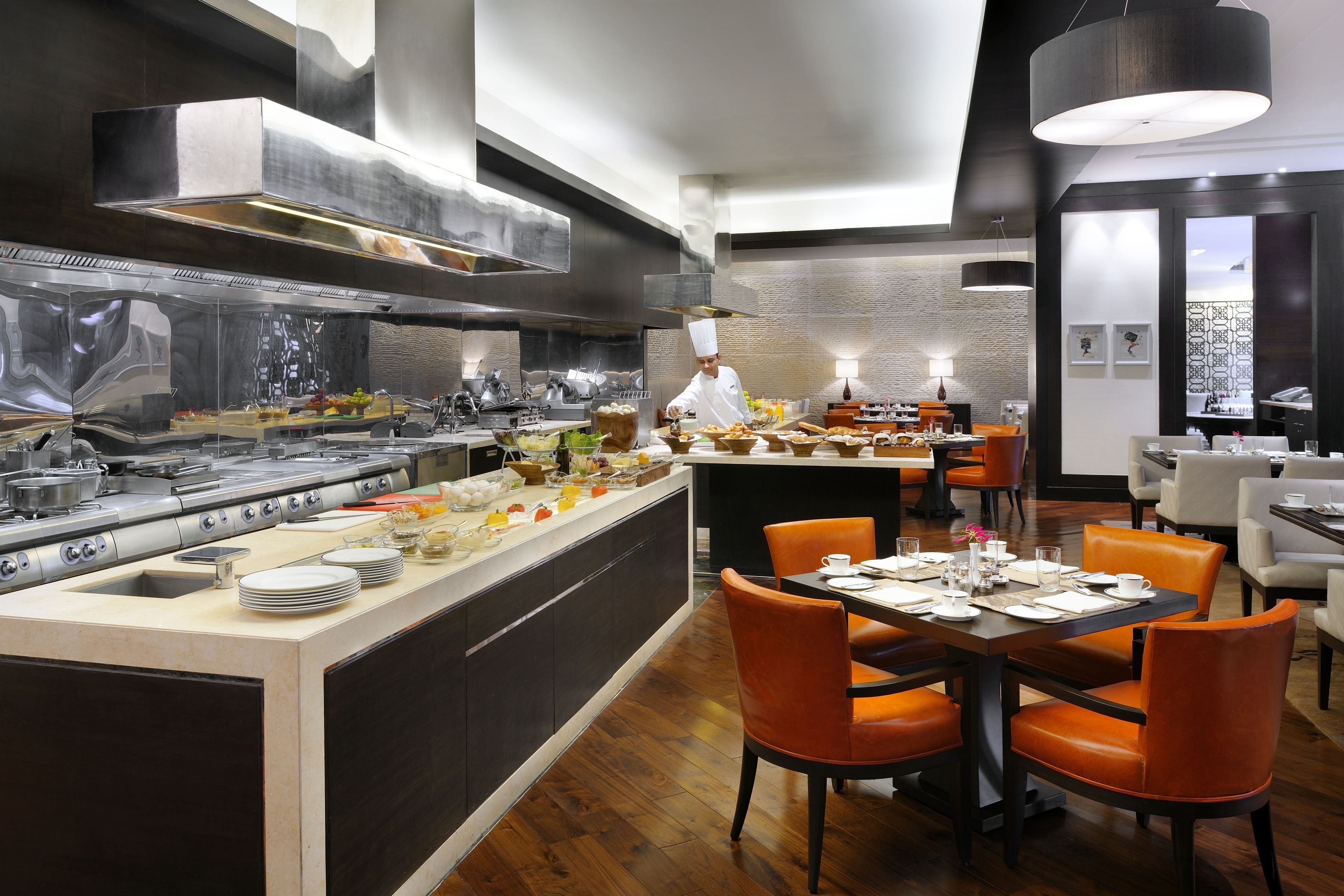 Un restaurante moderno con una isla central, sillas anaranjadas y un chef preparando comida.