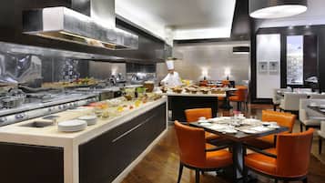 Ein modernes Restaurant mit einer zentralen Kochinsel, orangefarbenen Stühlen und einem Koch, der zubereitet.