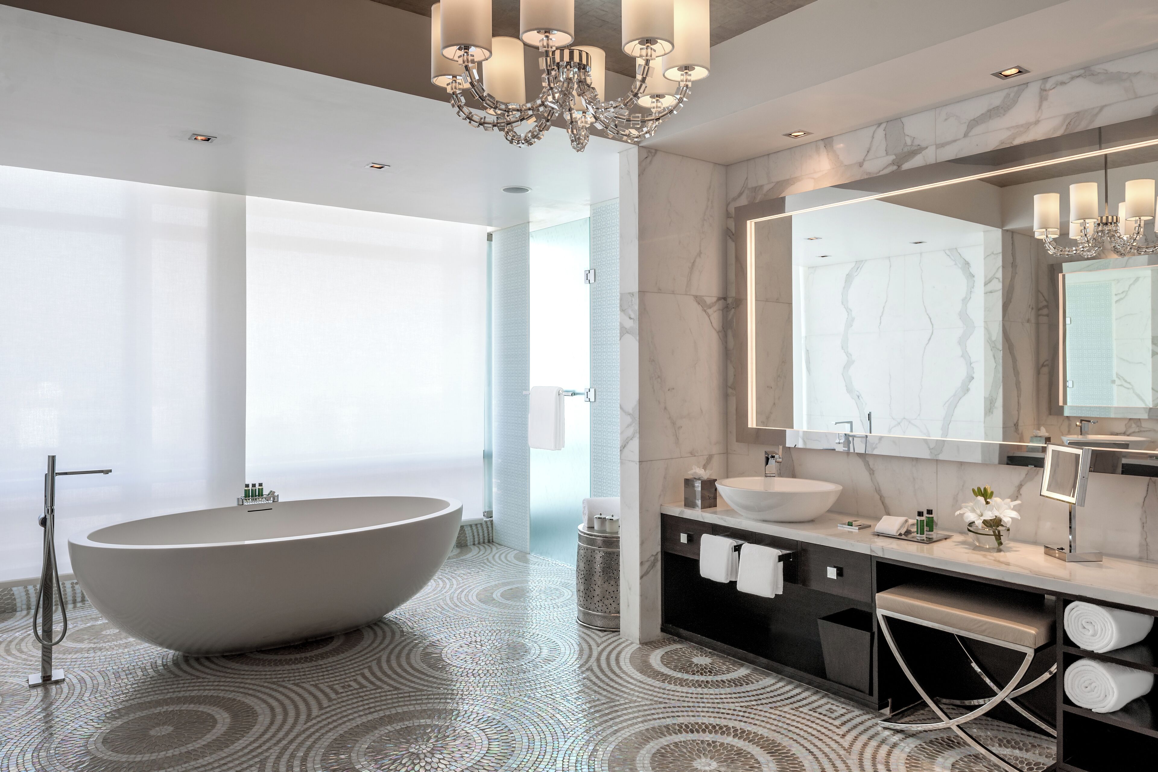A modern bathroom with a freestanding bathtub, a large mirror, and a chandelier.