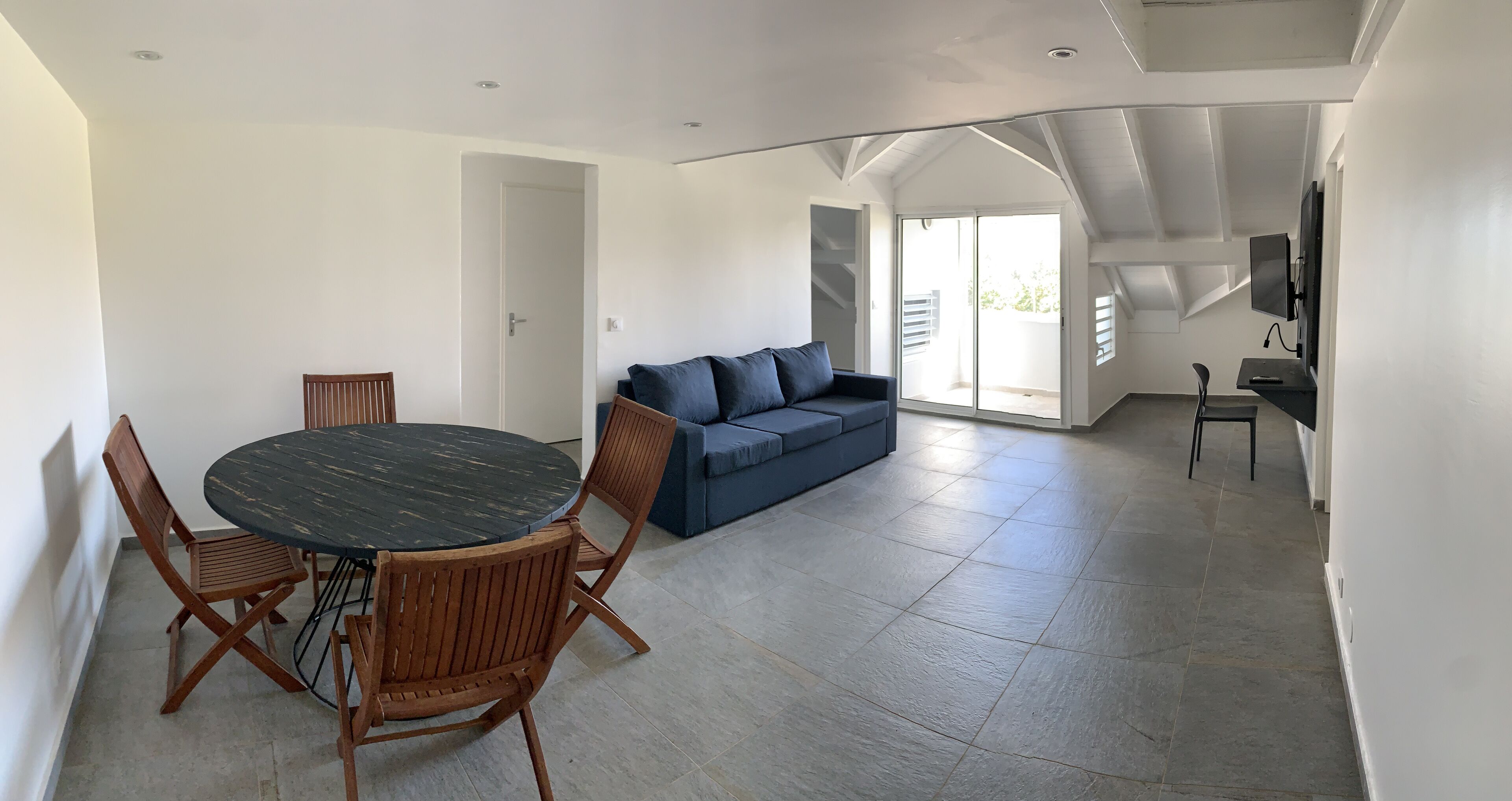 A spacious living area with a round wooden table and chairs, a blue sofa, and a television.