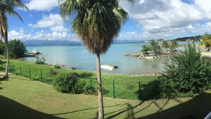 A coastal view with a clear sky, palm trees, and boats on the water. - Karaibes Residence (Le Gosier)