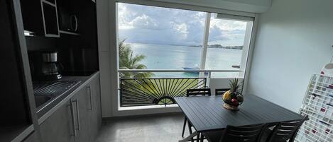 Una cocina con un gran ventanal con vistas a un cuerpo de agua, una mesa de comedor con sillas y un frutero sobre la mesa.