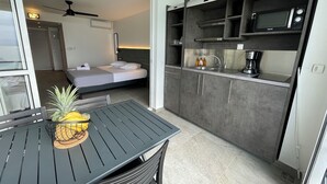 A compact kitchen with a microwave, coffee maker, and a small sink. A bed is visible in the adjacent room. - Karaibes Residence (Le Gosier)