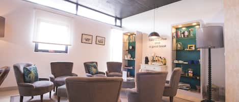 A cozy living room with multiple armchairs, a coffee station, and a bookshelf.