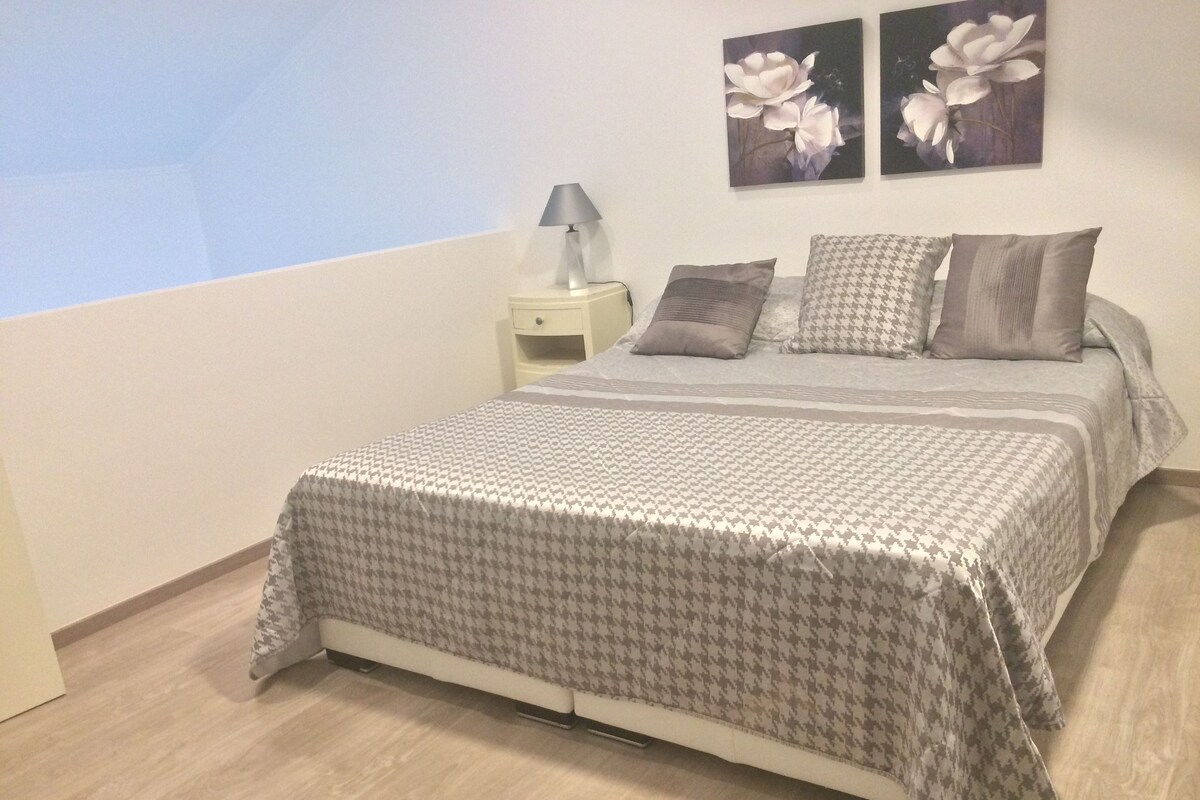 Une chambre à coucher avec une couvre-lit à motifs pied-de-poule, une table de chevet avec une lampe et deux tableaux floraux accrochés au mur.