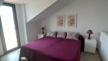A bedroom with a sloped ceiling, a bed with a purple bedspread, two bedside lamps, and two framed pictures on the wall.