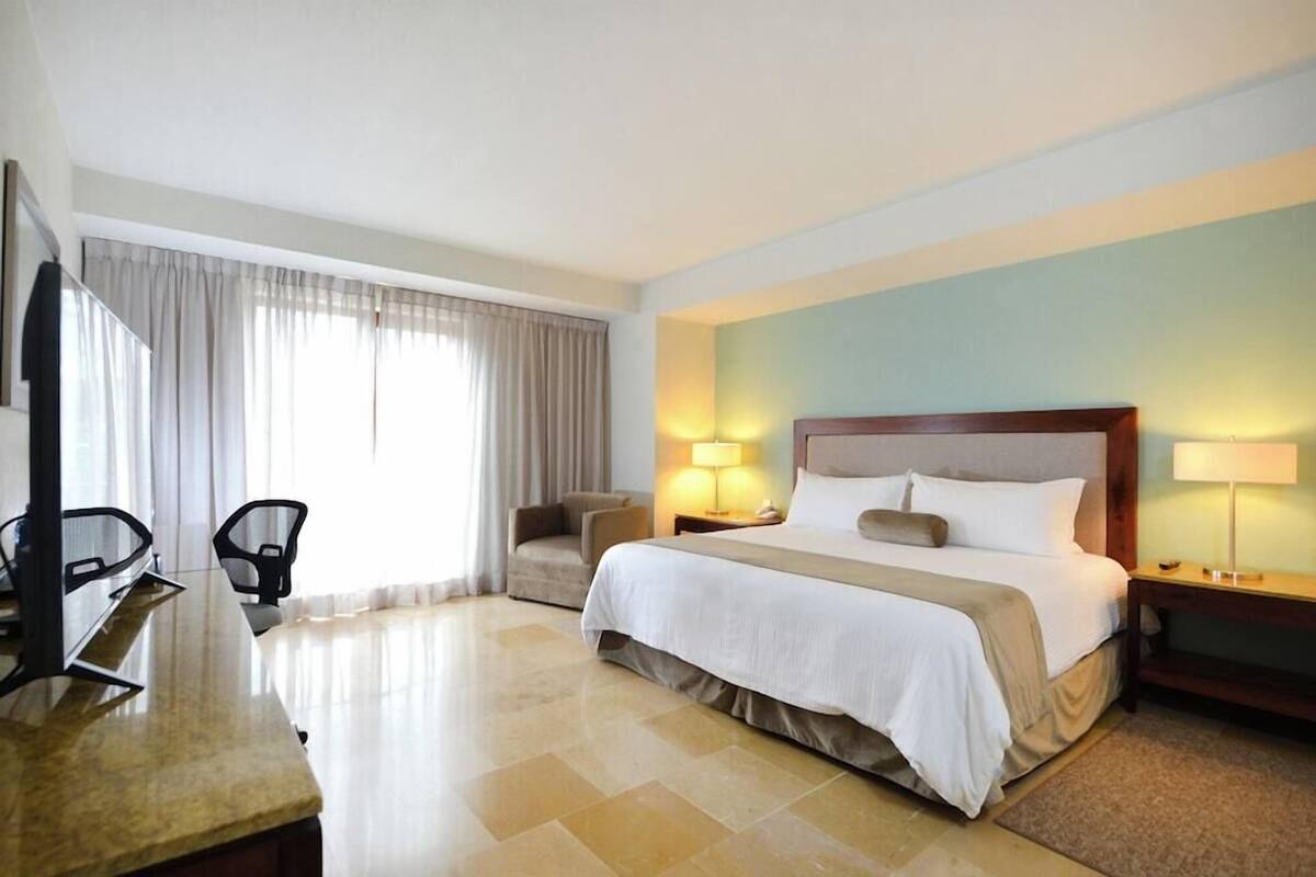 Ein Hotelzimmer mit einem Bett, zwei Stühlen, einem Schreibtisch und einem Fernseher.
