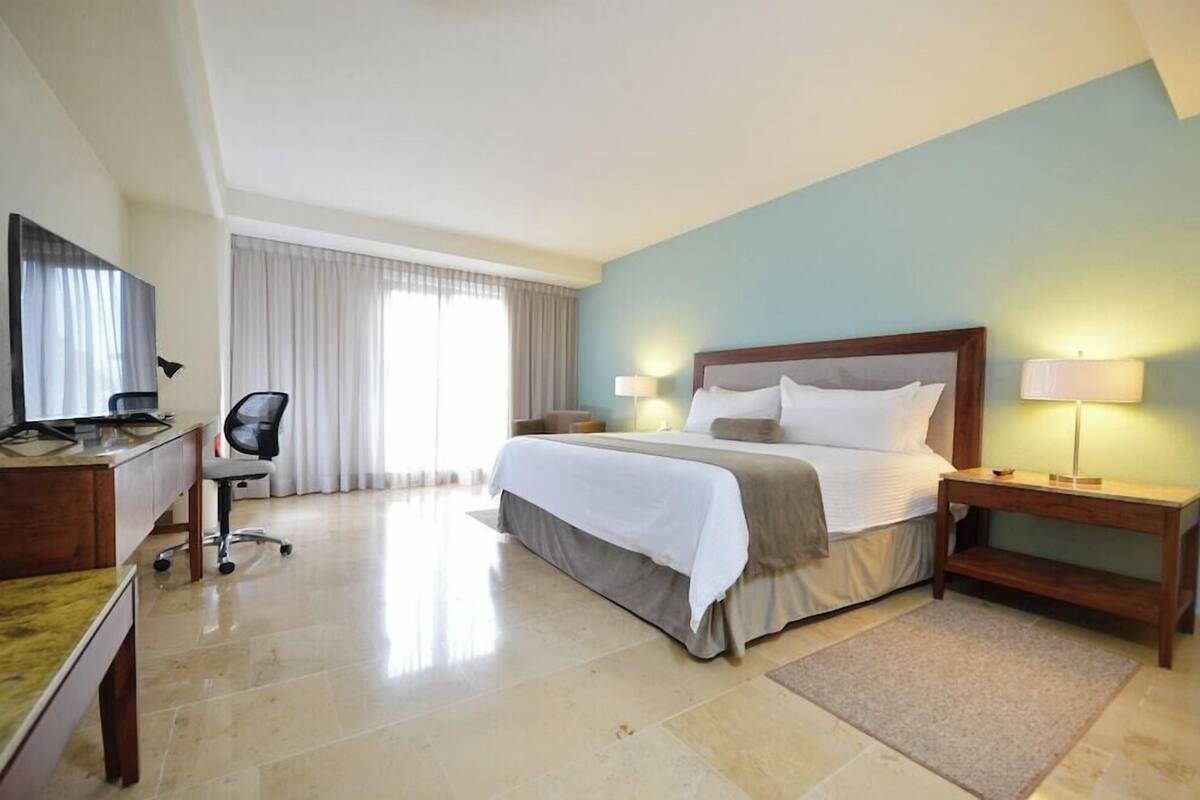 Ein Hotelzimmer mit Bett, Schreibtisch, Stuhl und einem großen Fenster mit Vorhängen.