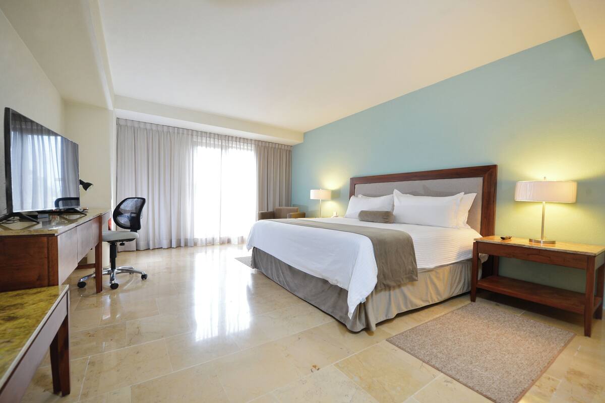 Ein Hotelzimmer mit Bett, Schreibtisch, Stuhl und einem großen Fenster mit Vorhängen.