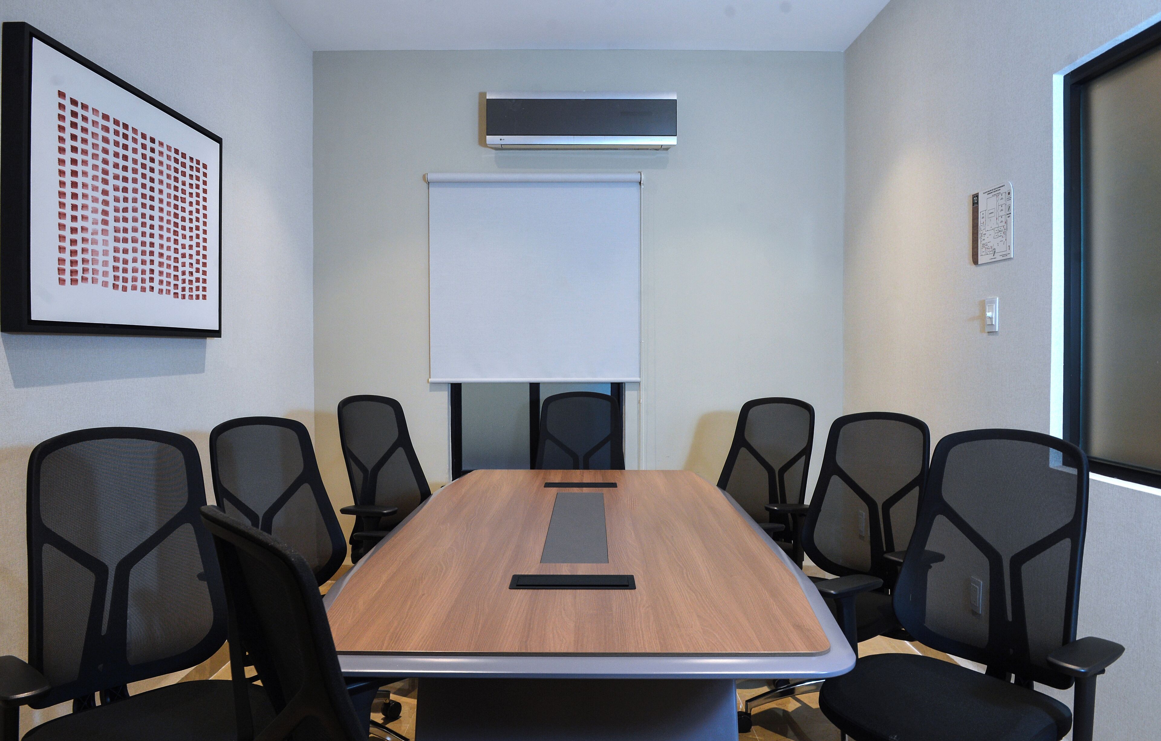 A conference room with a long table, six chairs, a whiteboard, and an air conditioning unit on the wall.