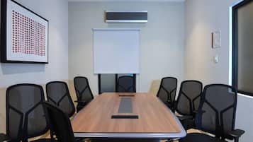 Un salón de conferencias con una larga mesa, seis sillas, una pizarra y un equipo de aire acondicionado en la pared.