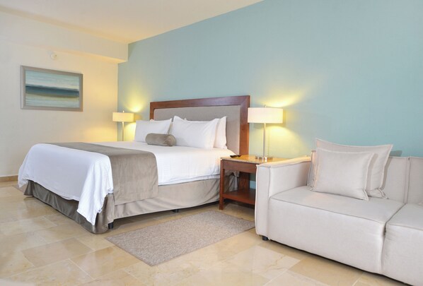 Una habitación de hotel con cama, mesita de noche con lámparas, sofá y un cuadro en la pared.