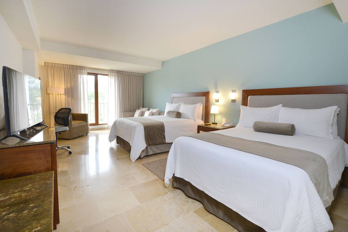 Ein Hotelzimmer mit zwei Betten, einem Schreibtisch mit Computer, einem Stuhl und einem Fernseher.