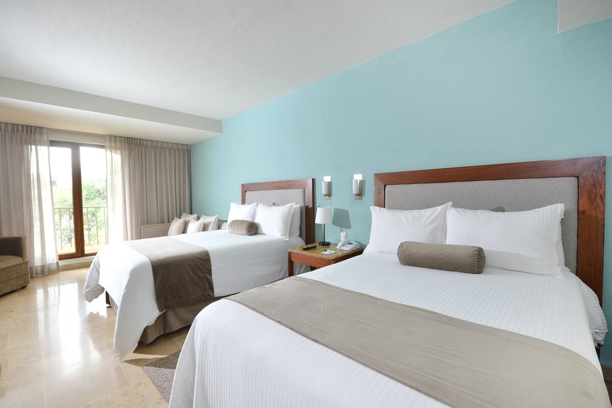 Ein Hotelzimmer mit zwei Betten, einem Sofa und einem Fenster mit Vorhängen.