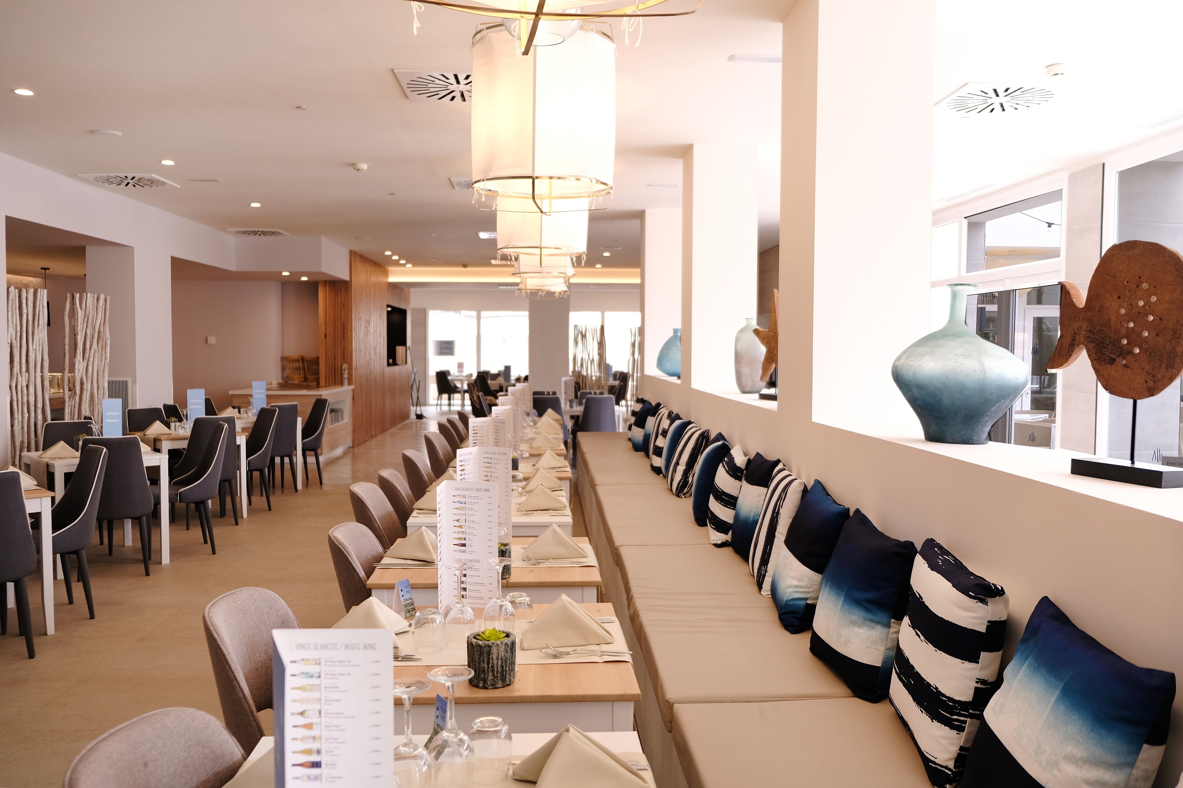 Un comedor moderno con mesas largas, sillas y un rincón de estar con cojines.