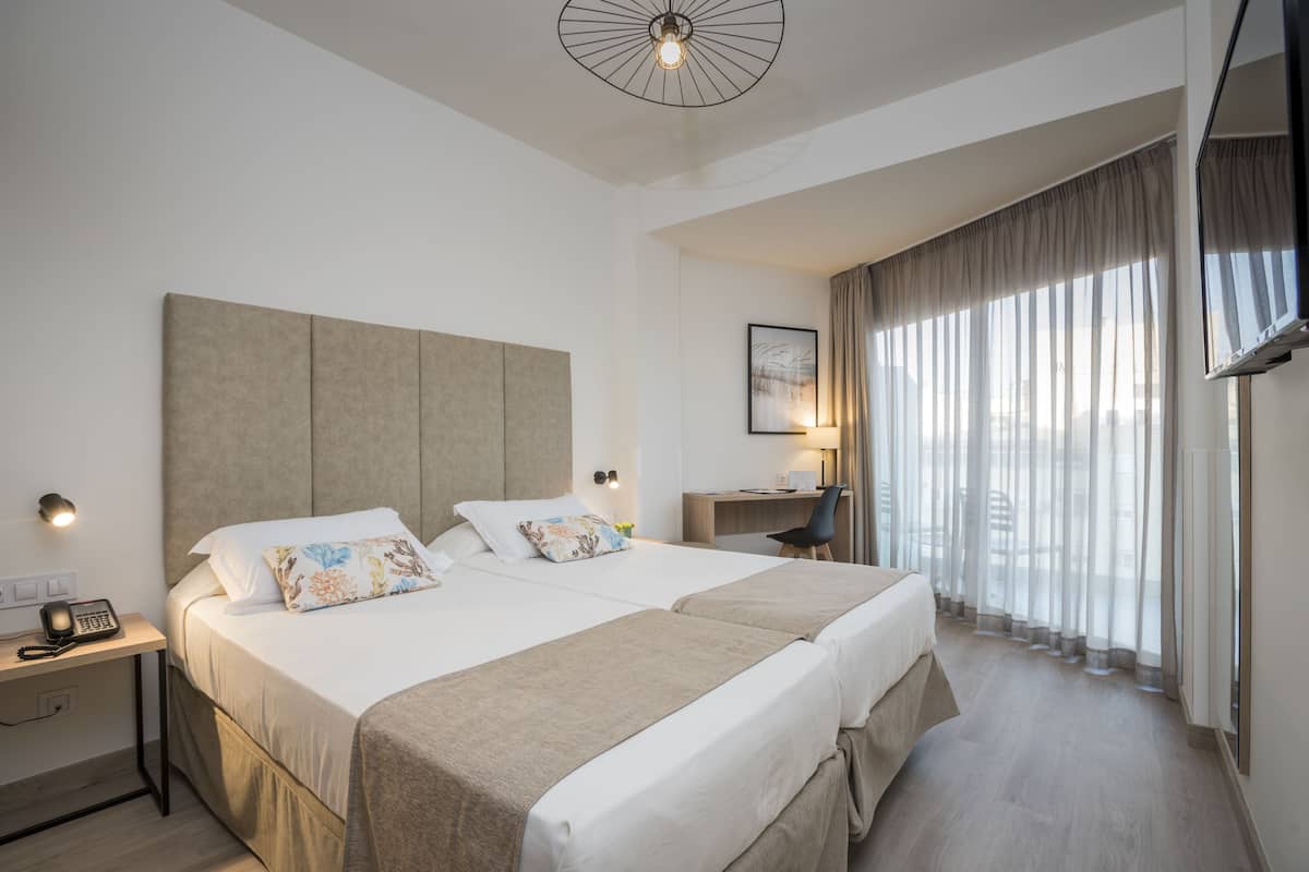 Una moderna camera d'hotel con un letto grande, una scrivania e vista sulla città attraverso tende leggere.