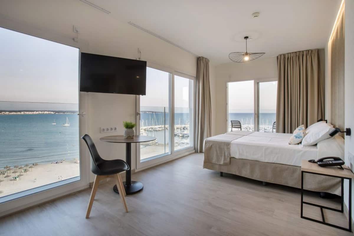 Una camera d'albergo con un letto, una scrivania, una sedia, una TV e vista sul mare.