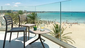 A balcony with two chairs and a table, overlooking a beach with people and boats. - Hotel Las Arenas (Palma de Mallorca)