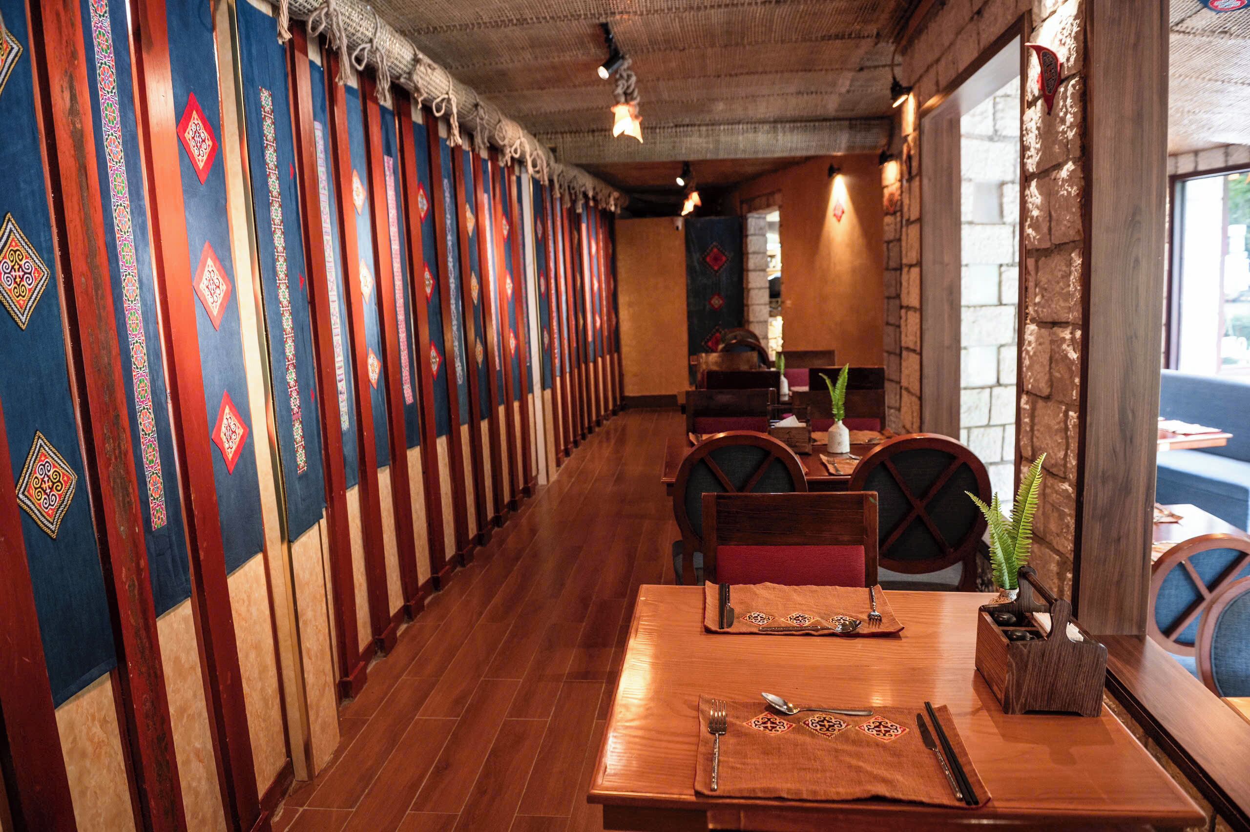 A restaurant with wooden tables and chairs, a long counter, and colorful wall hangings.