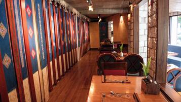 A restaurant with wooden tables and chairs, a long counter, and colorful wall hangings.