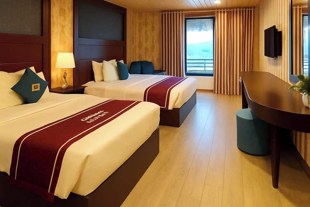 A hotel room with two beds, a desk, a TV, and a large window with curtains.