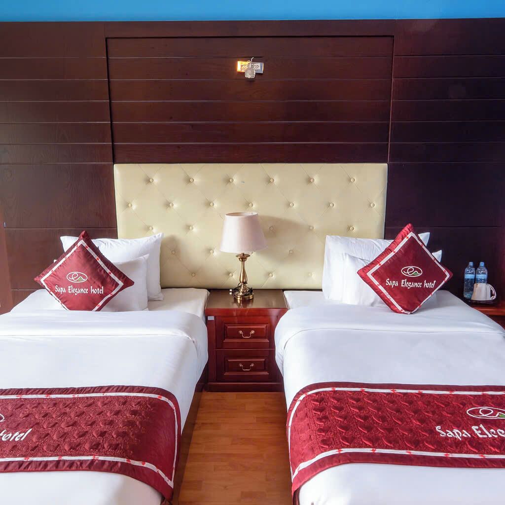 A hotel room with two beds, a nightstand, a lamp, and a minibar.