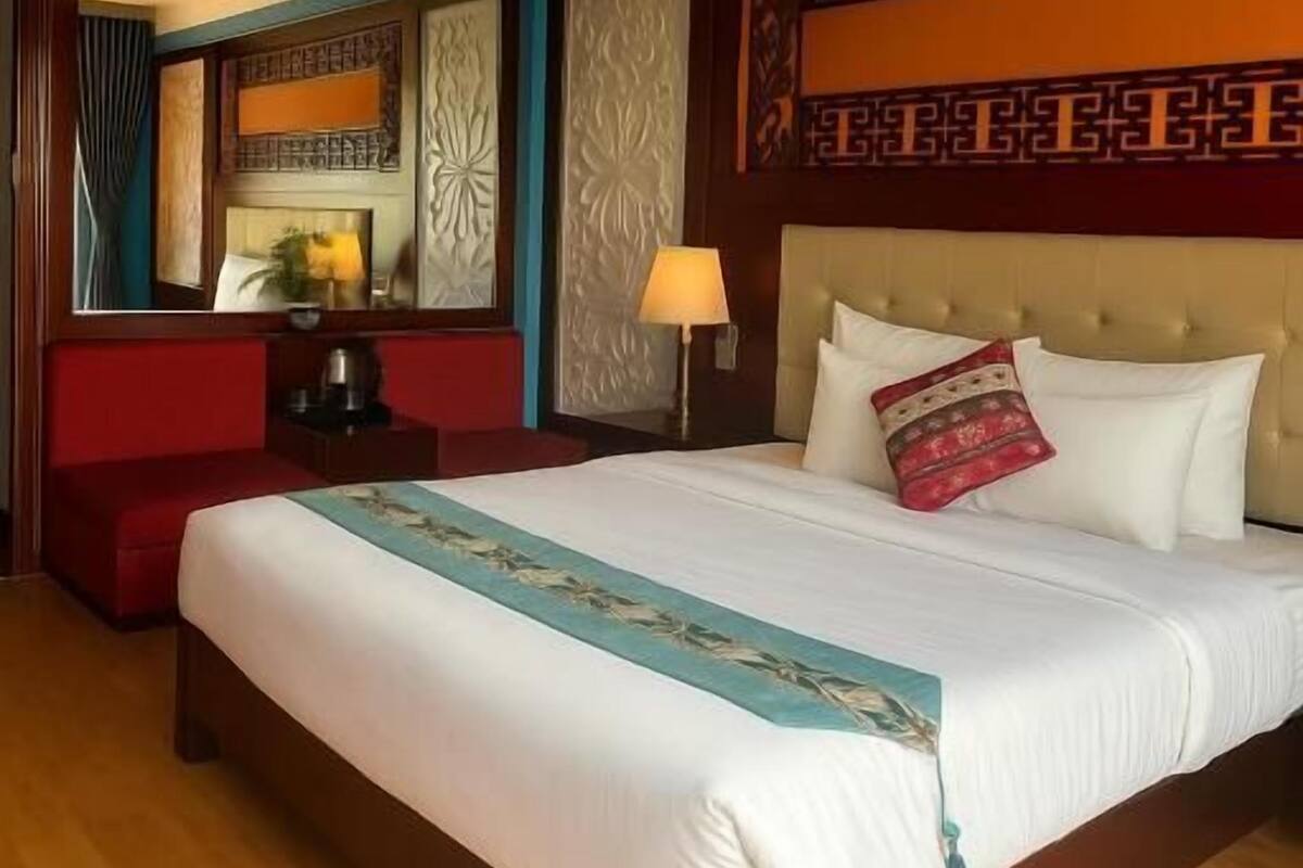 A hotel room with a large bed, a red sofa, a nightstand, and a mirror.
