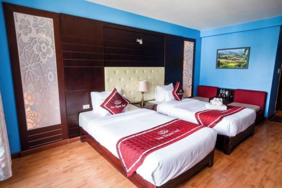 A hotel room with two beds, a large headboard, a decorative panel, a nightstand, and a painting on the wall.