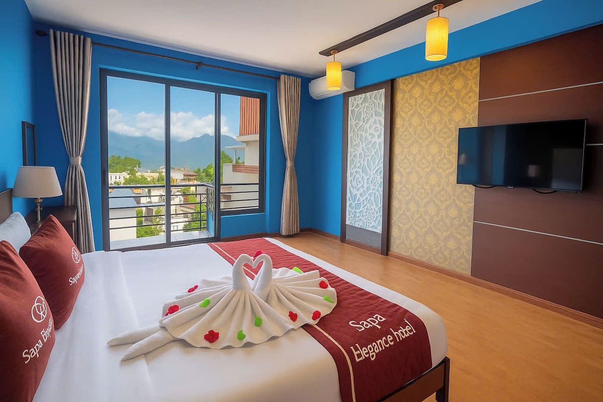 A hotel room with a large bed, a TV mounted on the wall, and a view of the city through the window.