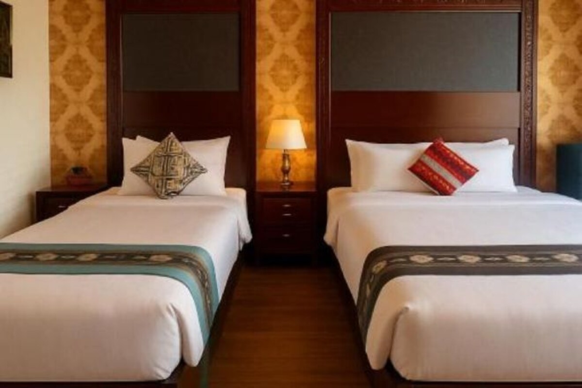 A hotel room with two beds, each with a wooden headboard, a bedside table, and a lamp.