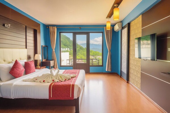 A hotel room with a bed, curtains, a TV, and a view of greenery outside.