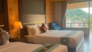 Habitación de hotel con dos camas, una mesita de noche con lámpara, una silla y un ventanal con vistas a una montaña.