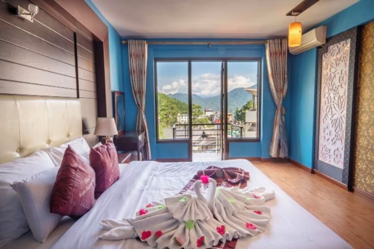 A hotel room with a bed, a view of mountains, and a balcony.