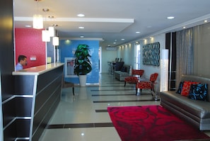 A hotel reception area with a reception desk, a potted plant, a seating area with chairs, and a sofa. - Metro Hotel Panama (Panama City)