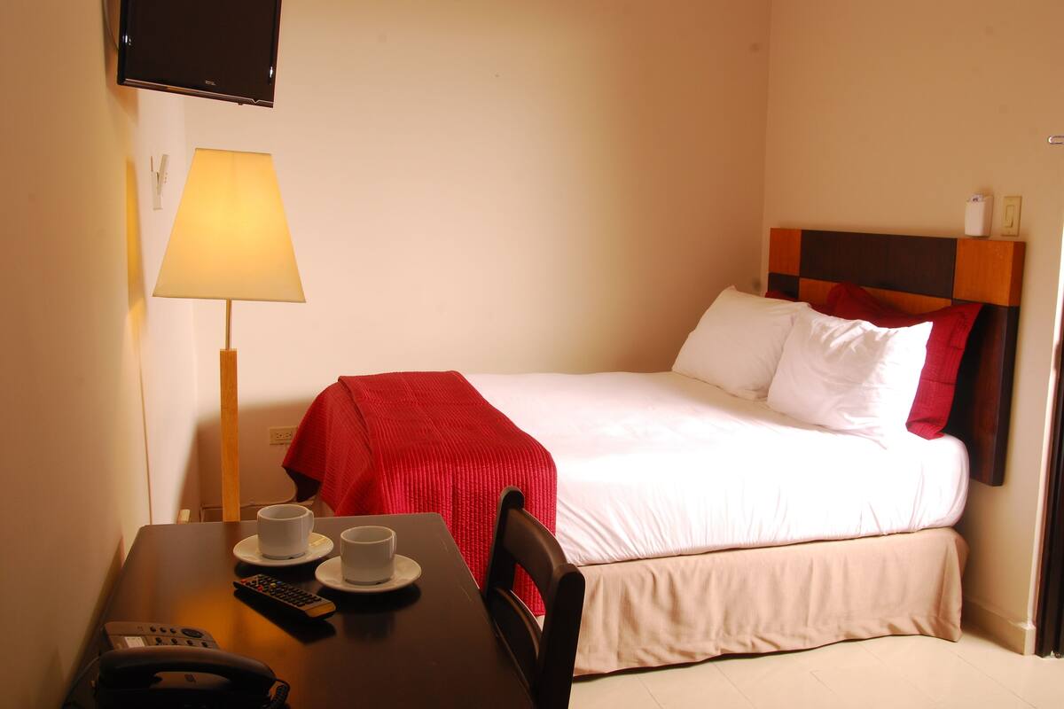 Et hotelværelse med en seng, et bord med en lampe, en telefon og to kopper.