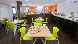 A modern dining area with bright green chairs and tables, a kitchen counter with various food items, and a large window providing natural light. - Metro Hotel Panama (Panama City)