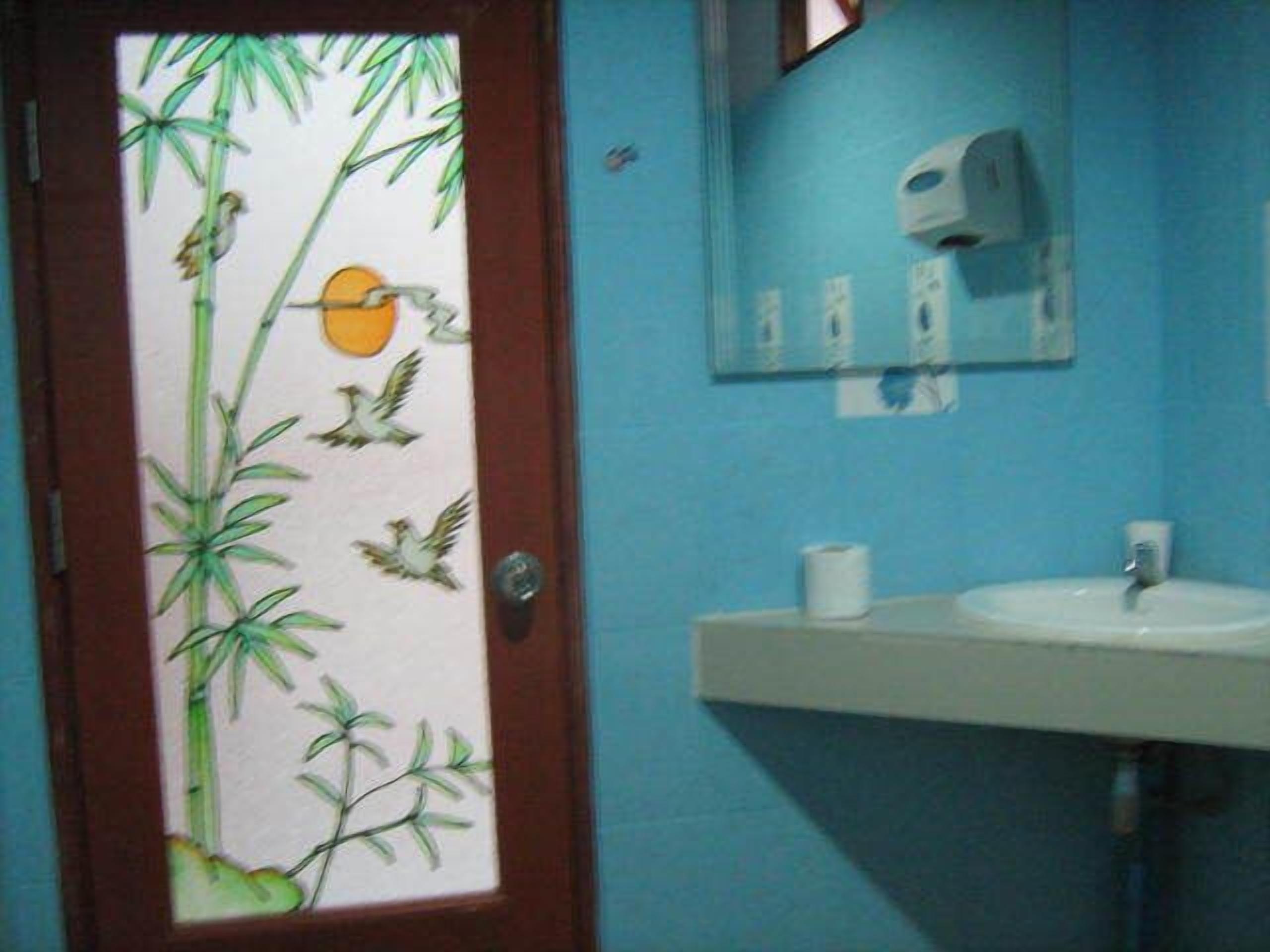 A bathroom with a blue wall, a white sink, and a door with a bamboo and bird design.