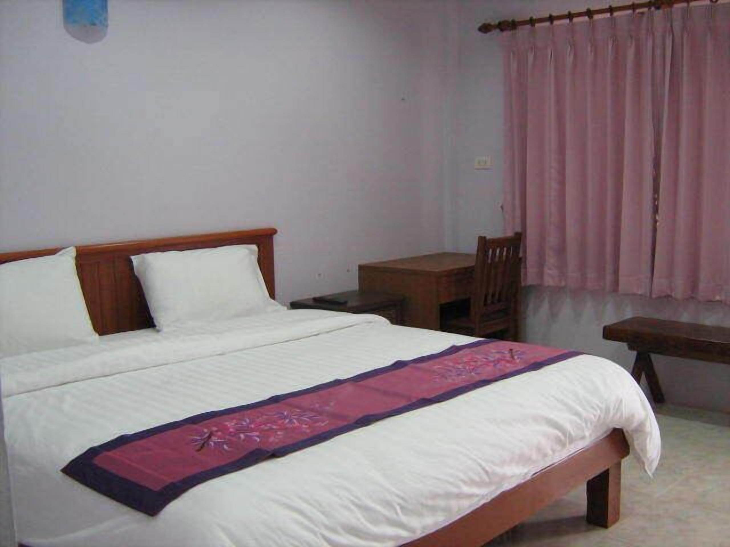 Un dormitorio con cama, cabecera de madera, mesita de noche, una silla y ventana con cortinas rosadas.