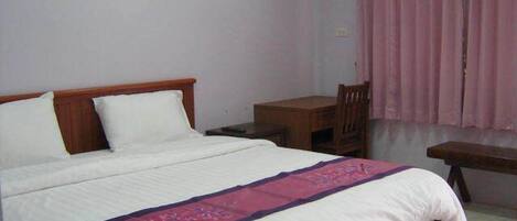 Un dormitorio con cama, cabecera de madera, mesita de noche, una silla y ventana con cortinas rosadas.