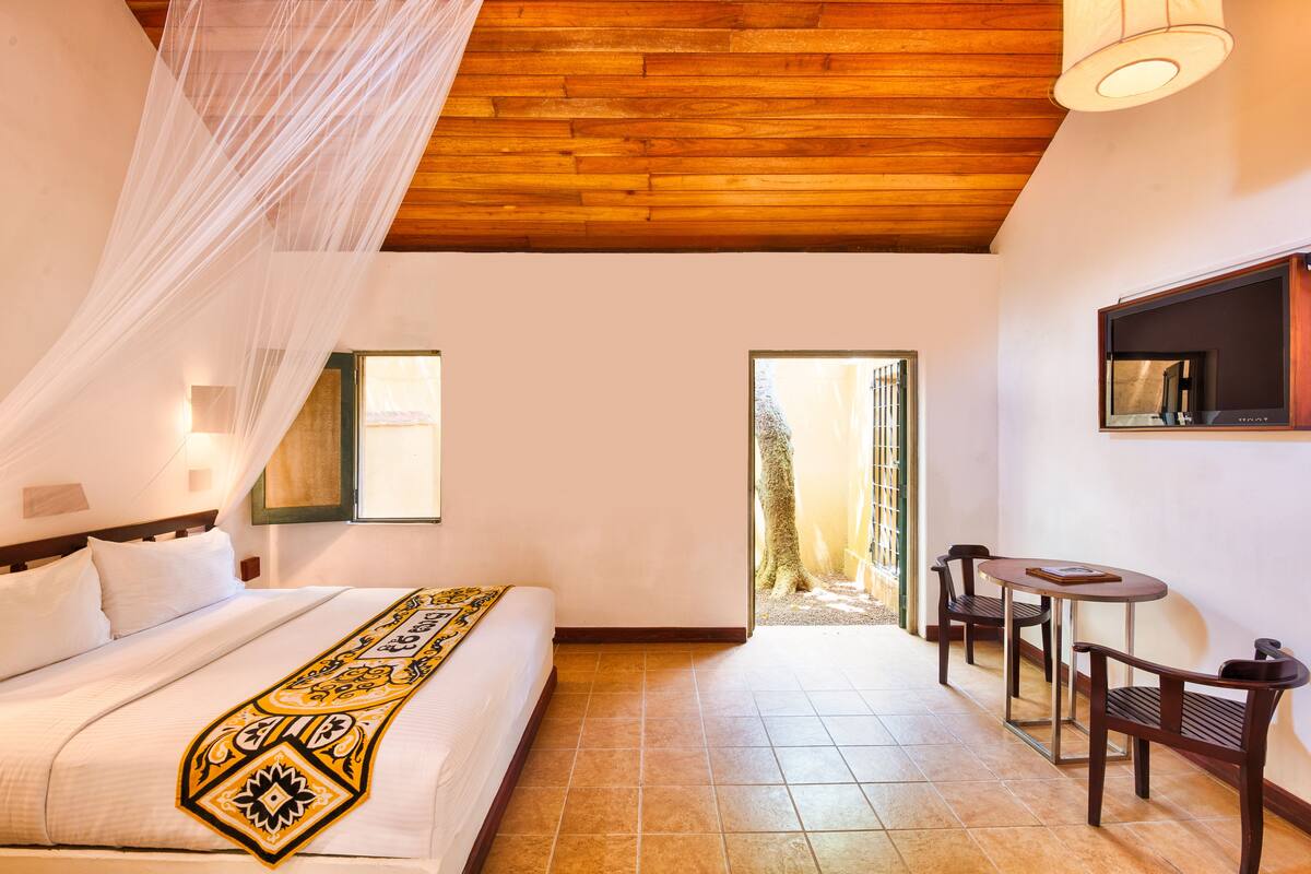 A bedroom with a bed, a bedside table, a chair, a TV, and a window.