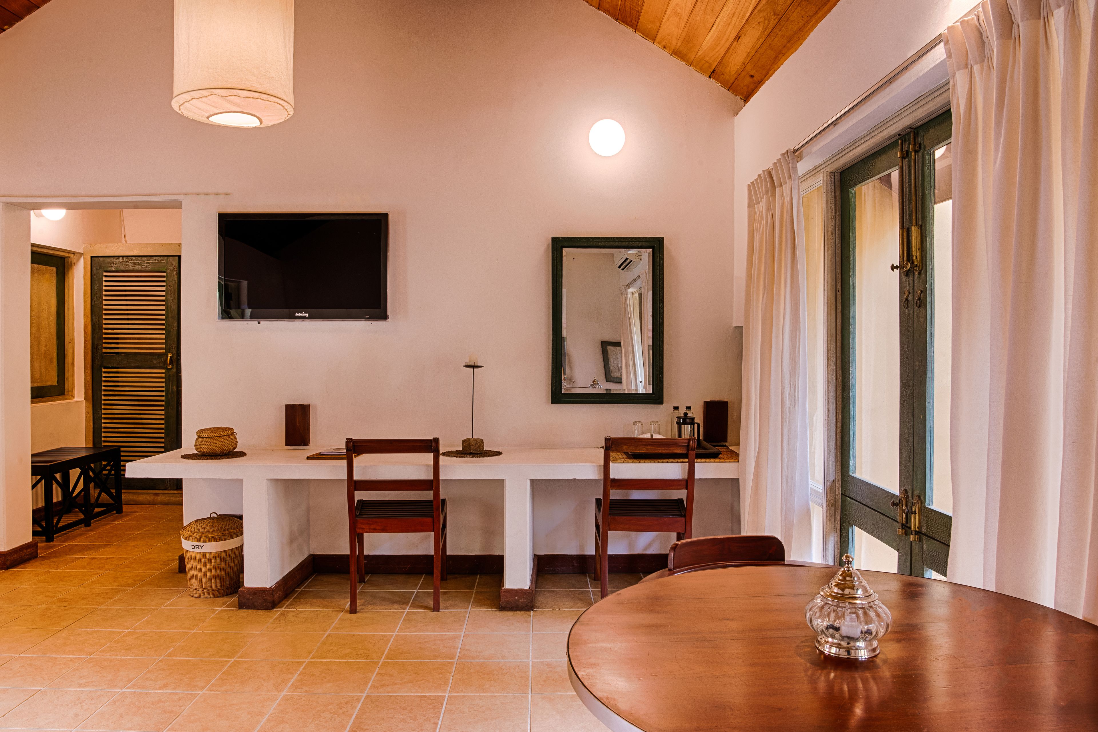 Un comedor con una mesa y sillas de madera, un televisor montado en la pared y un ventanal con cortinas.
