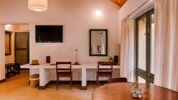 Un comedor con una mesa y sillas de madera, un televisor montado en la pared y un ventanal con cortinas.