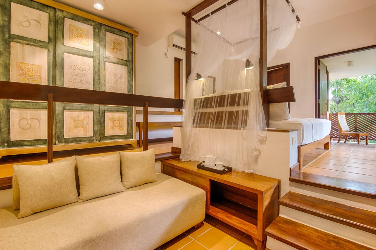 A bedroom with a bed, a sofa, a wooden bench, and a wall with framed artwork.